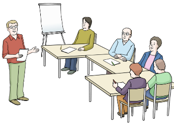 Auf dem Bild sieht man mehrere Menschen, die an einem Tisch sitzen. Vorne steht eine weiße Tafel. Neben dem Tisch steht ein Mann, der etwas erklärt.